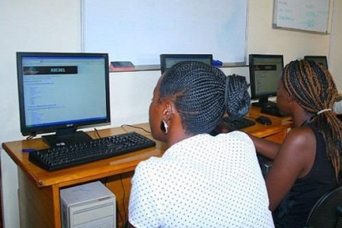 Two young African women work at desktop computers.