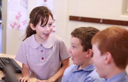 Three smiling young learners in a computing classroom.
