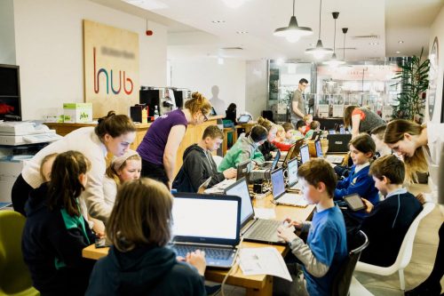 Photo: children and teenagers work on laptops at a CoderDojo, while adults help