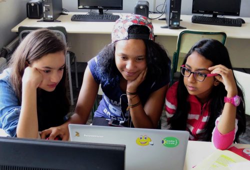 Three girls, all concentrating, one smiling, work together at a computer at Code Club