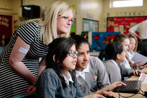 A teacher watches two female learners code in Code Club session in the classroom.