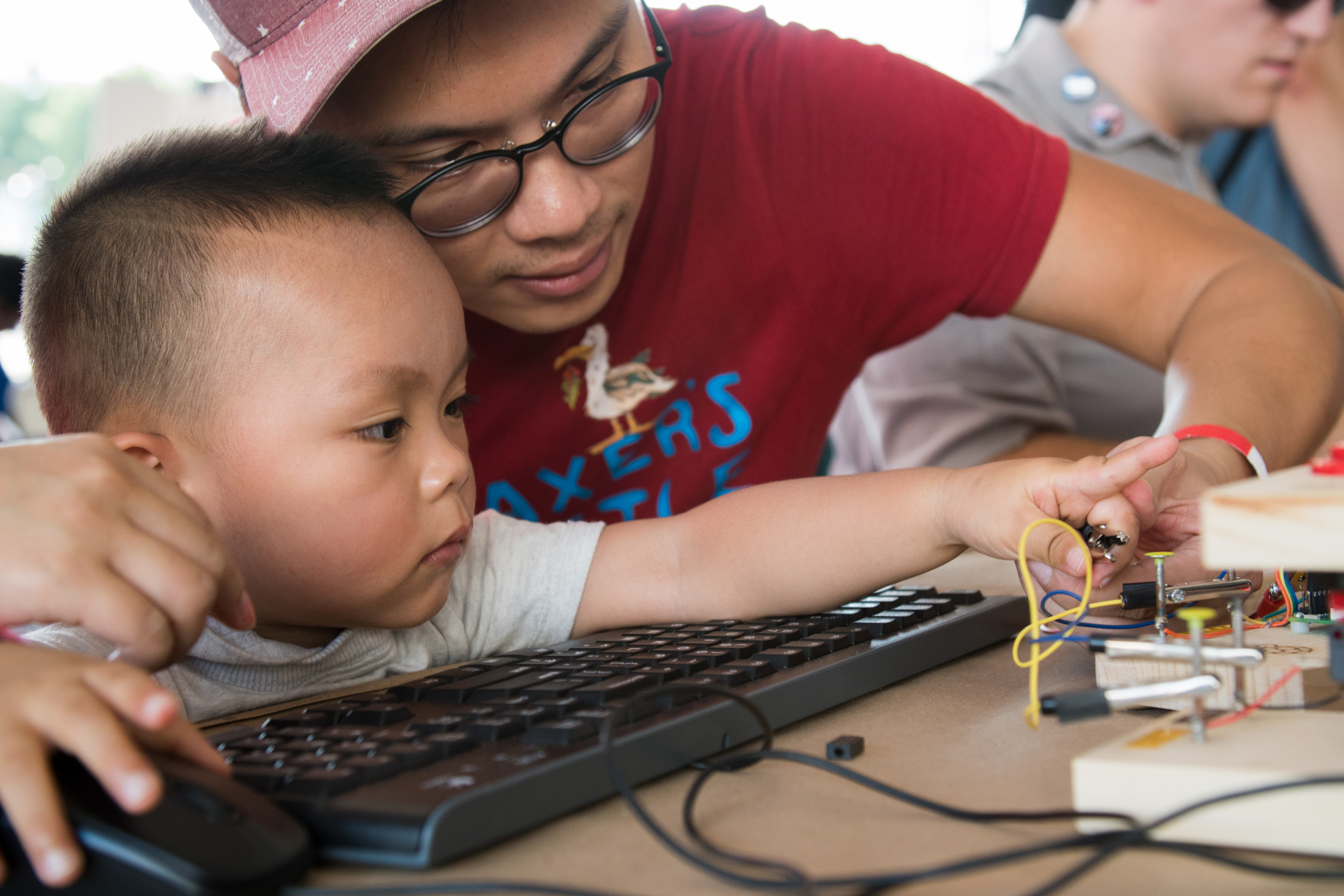 Father and infant child clip crocodile leads to the Raspberry Pi physical computing blocks at Maker Faire New York