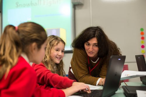 Two girls coding at a computer under supervision of a female teacher