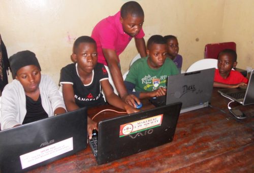 A man helps four young people to code projects at laptops in a CoderDojo session.