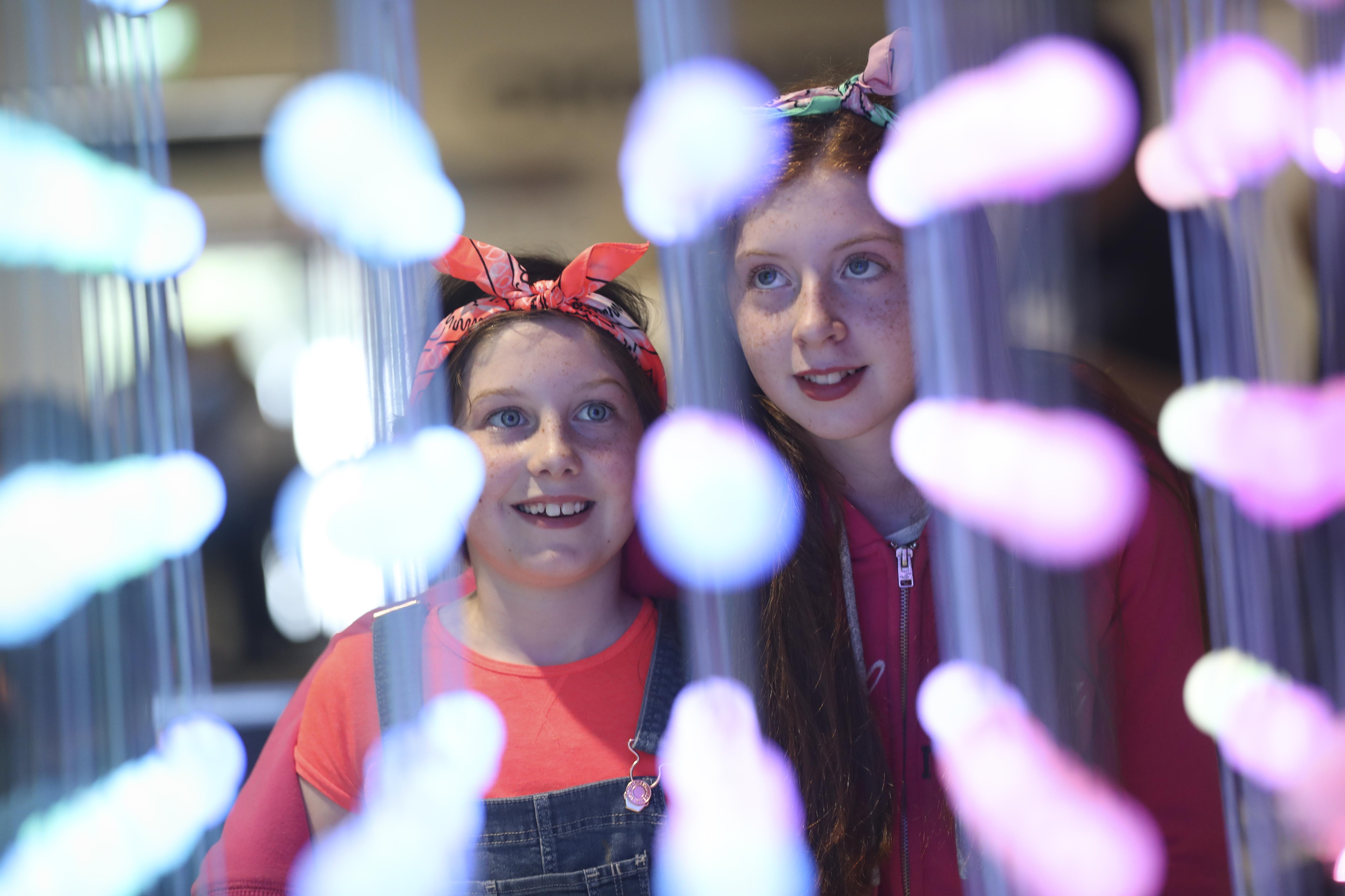 Two smiling girls observe a colourful LED arrangement