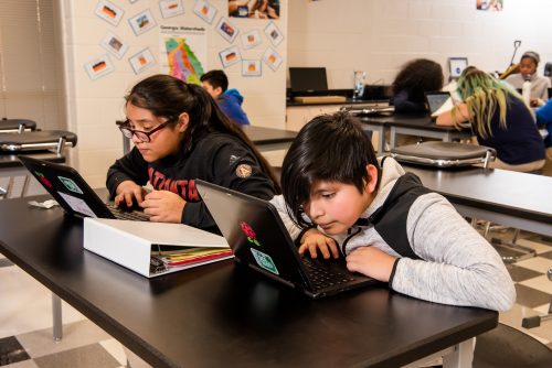 Two young people code at laptops.