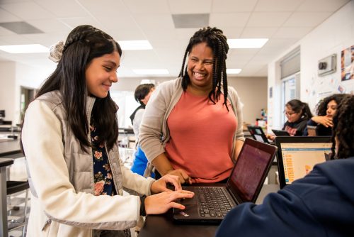 A teacher encourages a learner in the computing classroom.