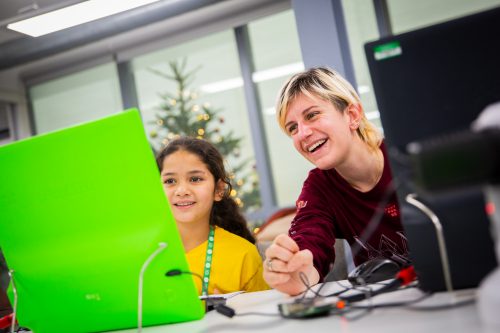 A women and a young girl sit side by side. They are concentrating on a screen connected to a Raspberry Pi and smiling widely