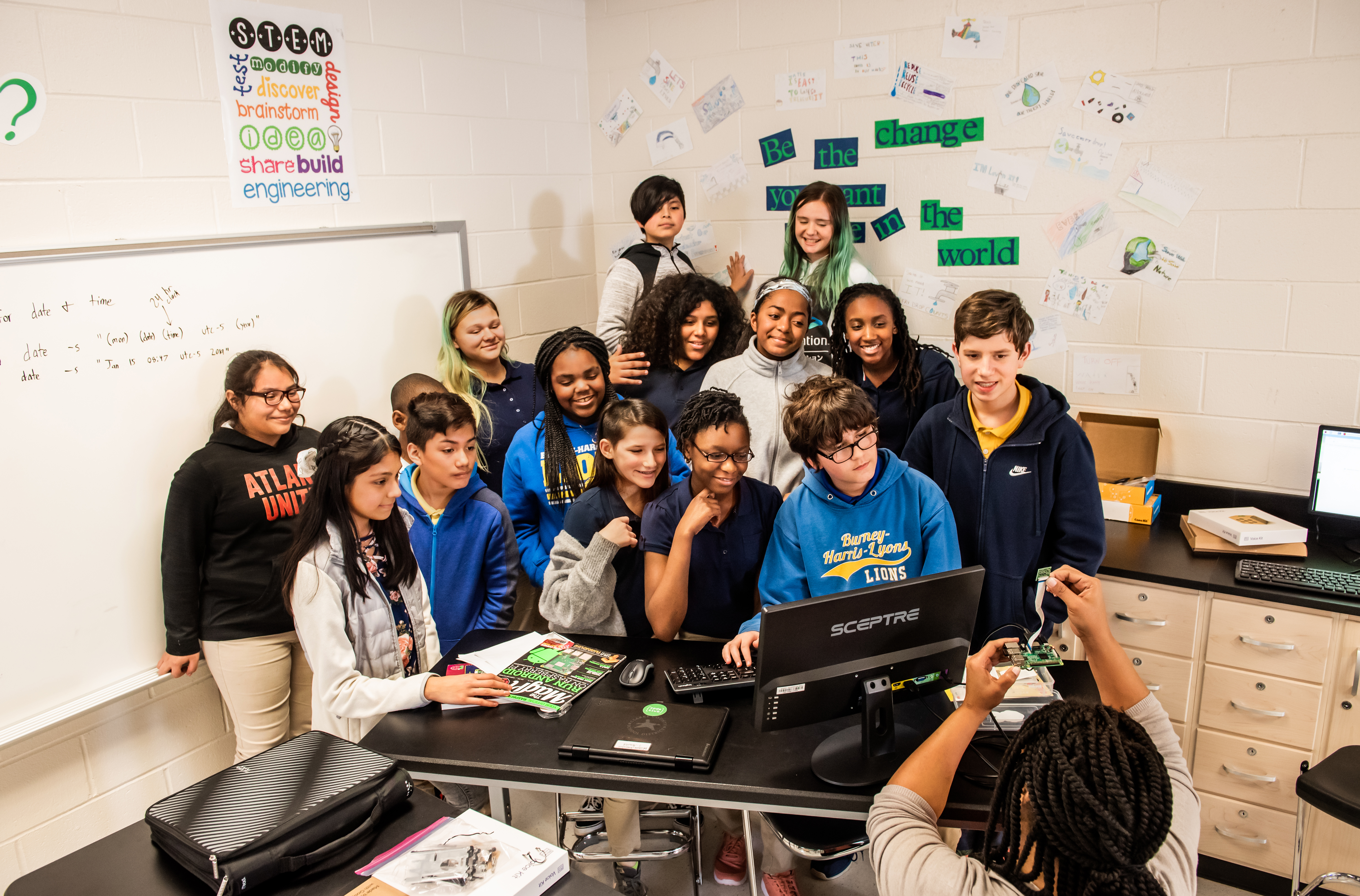 A group of young people in a computer science classroom pose for a group photo.