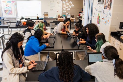 A classroom of young learners and a teacher at laptops