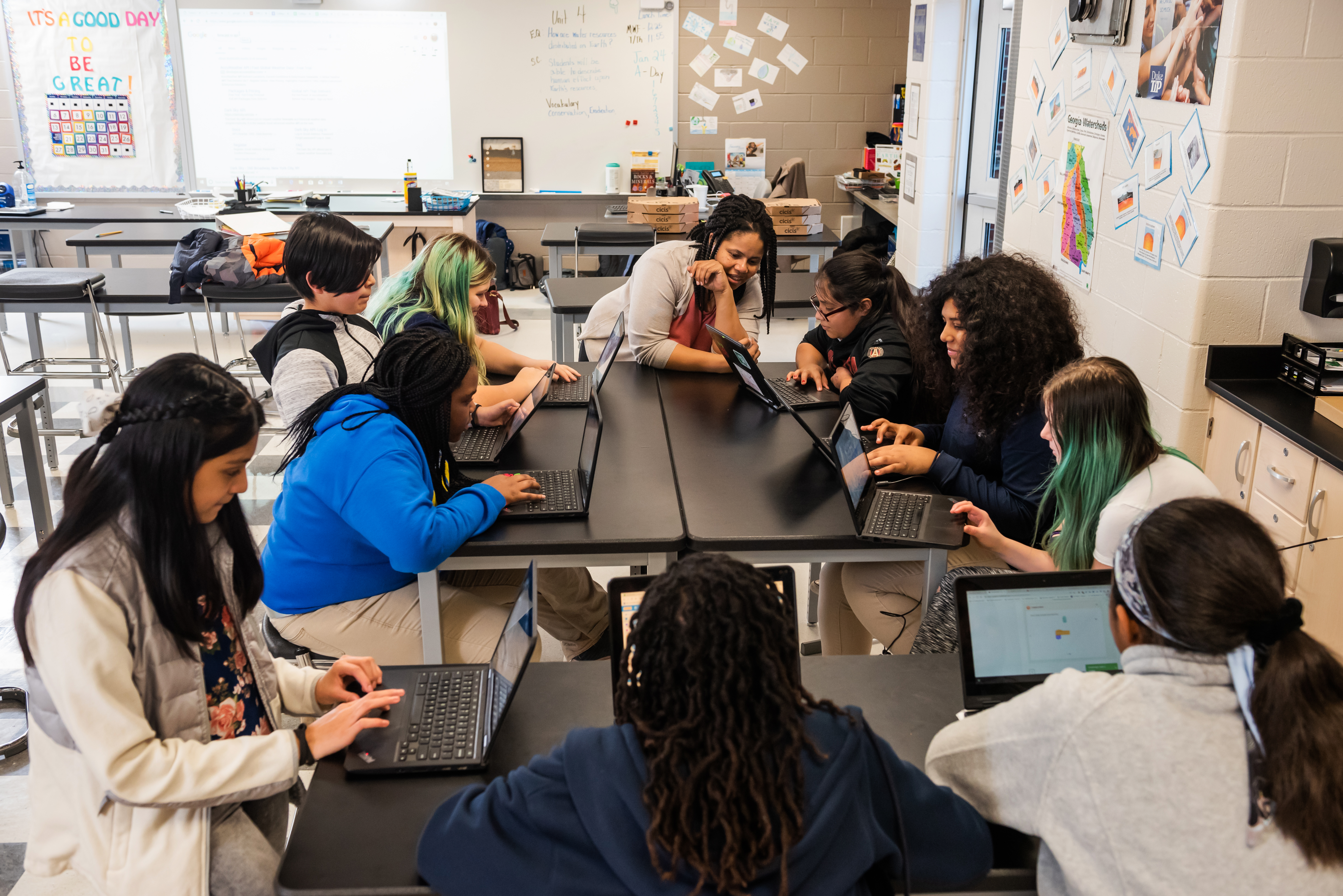 A classroom of young learners and a teacher at laptops