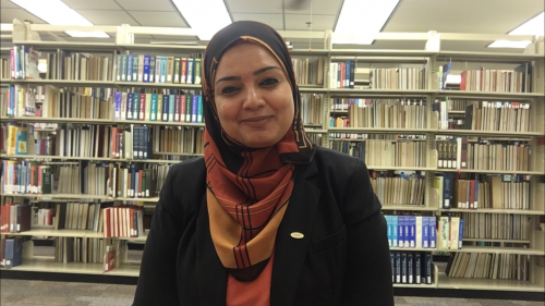 A woman wearing a headscarf standing in front of a library shelf