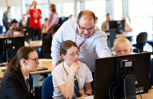A male teachers and three female students at a computer