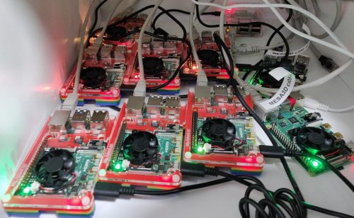 Ten Raspberry Pis with small black fans, most of them in colourful Pimoroni Pibow open cases, in a nest of cables and labels