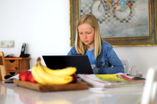 A girl does school work at a laptop at home.