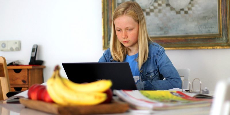 A girl does school work at a laptop at home.