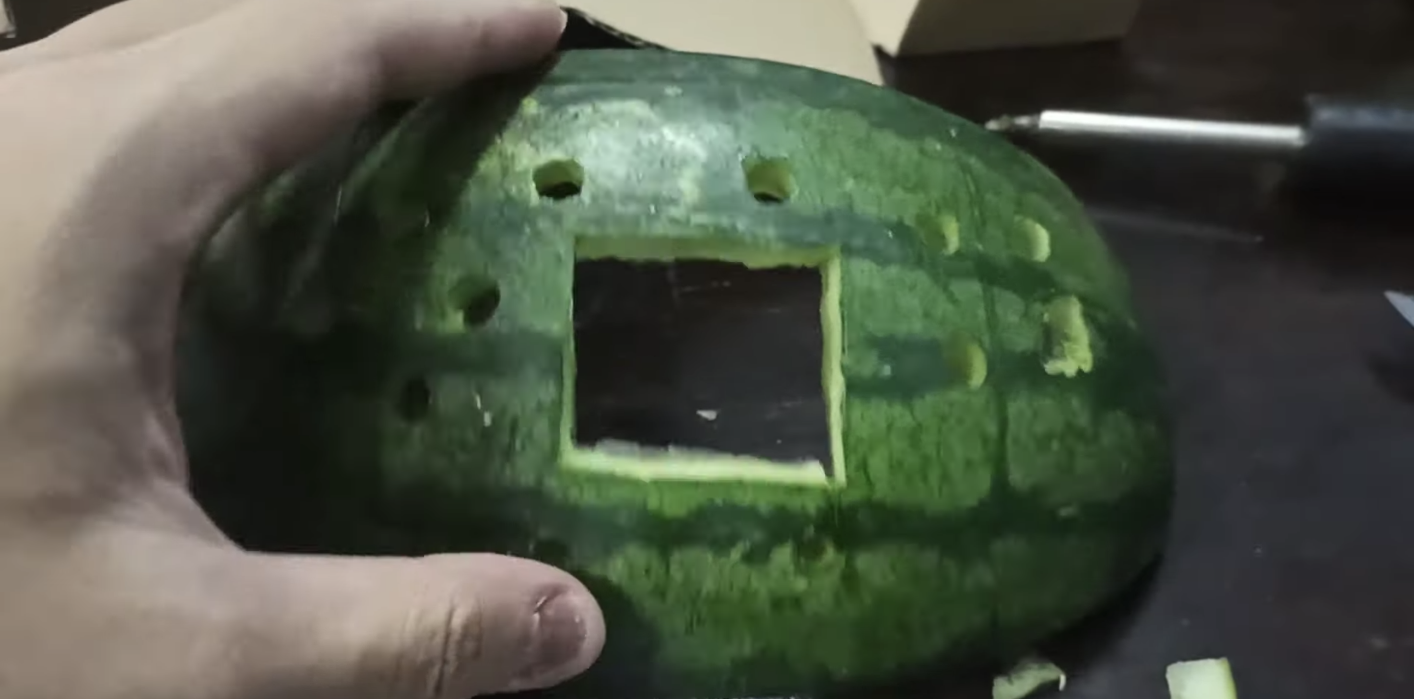 A gutted watermelon with gaps cut to fit games console buttons and a screen