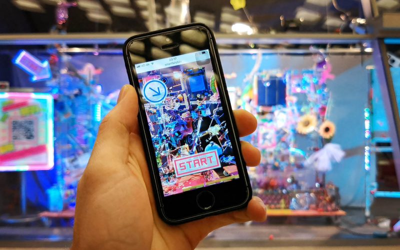 A phone using the app to control the installation. The installation is out of focus in the background