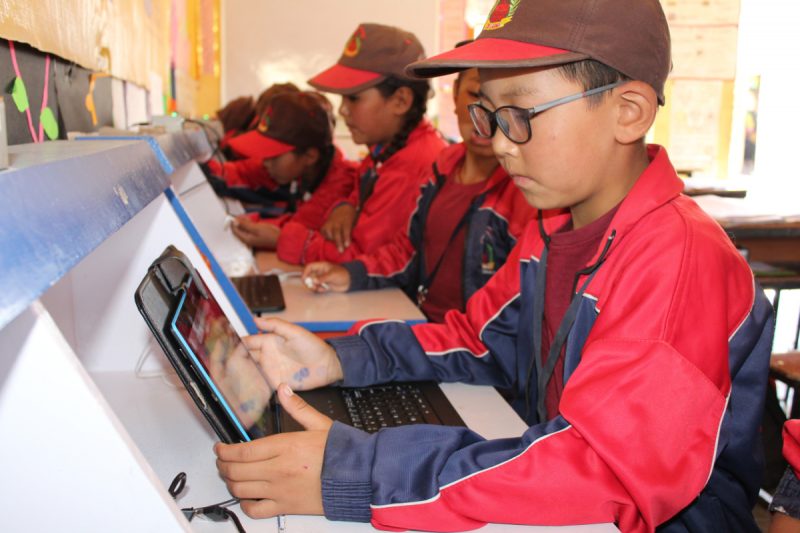 Young learners in red jackets and baseball caps using tablets to learn in a Himalayan school