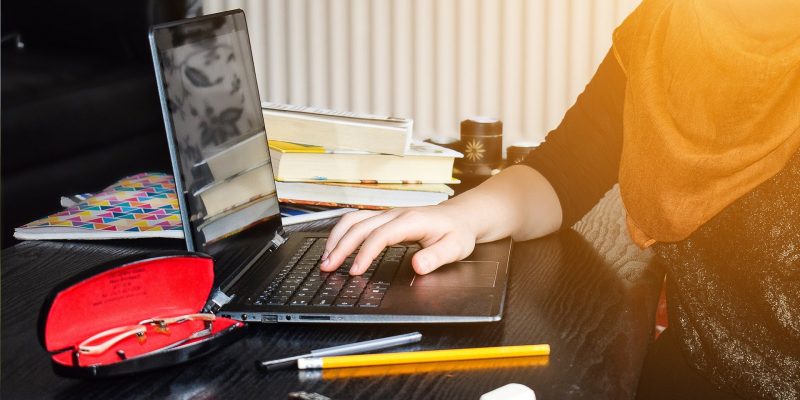 A girl in a hijab learning at home at a laptop