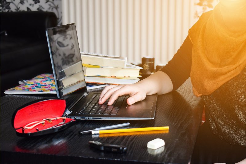 A girl in a hijab learning at home at a laptop