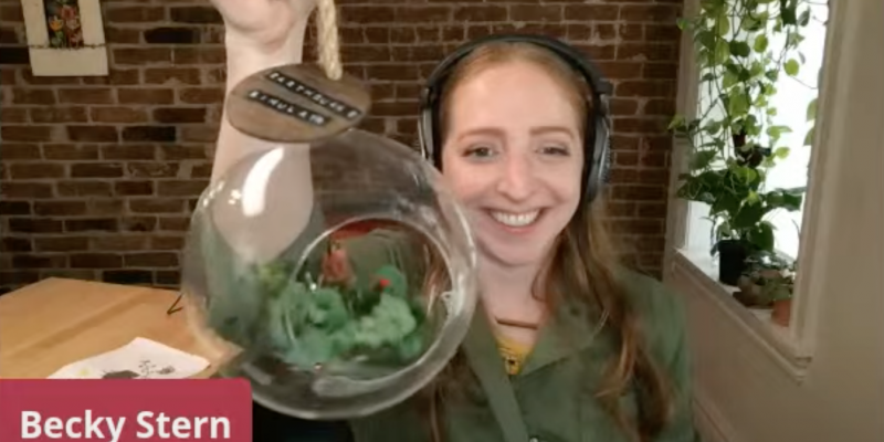 becky stern holding a project up to camera and smiling wearing headphones