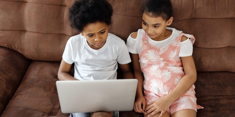 Two siblings sit on a sofa looking at a laptop