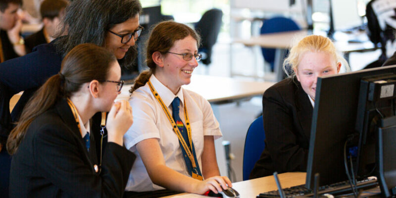 school-aged girls and a teacher using a computer together.