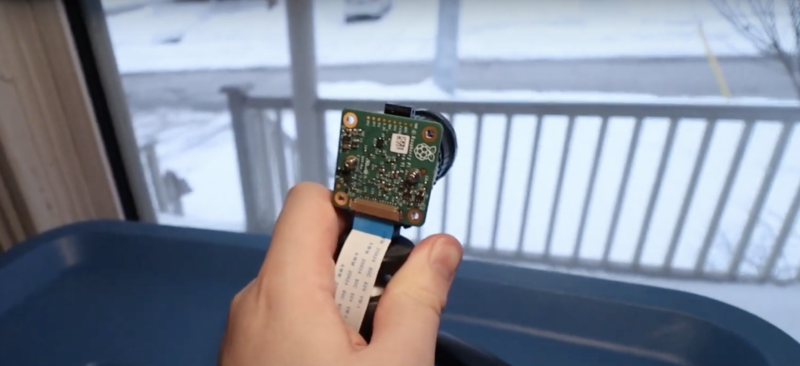 A hand holding a raspberry pi high quality camera pointing out of a window