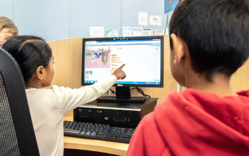 A young girl and boy do a Scratch coding activity together at a desktop computer.