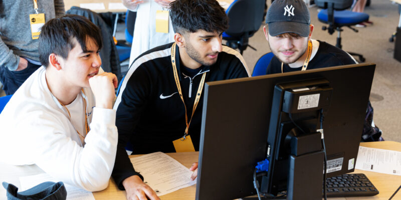 Three teenage boys do coding at a shared computer during a computer science lesson.