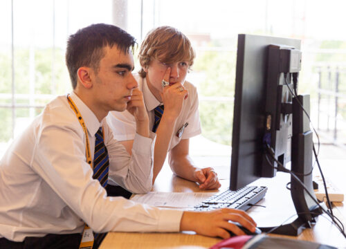 Two teenage boys do coding at a shared computer during a computer science lesson.