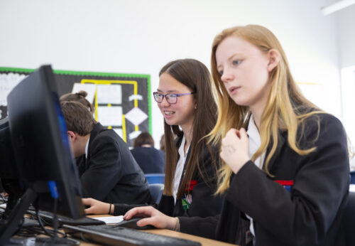 Two teenage girls do coding during a computer science lesson.