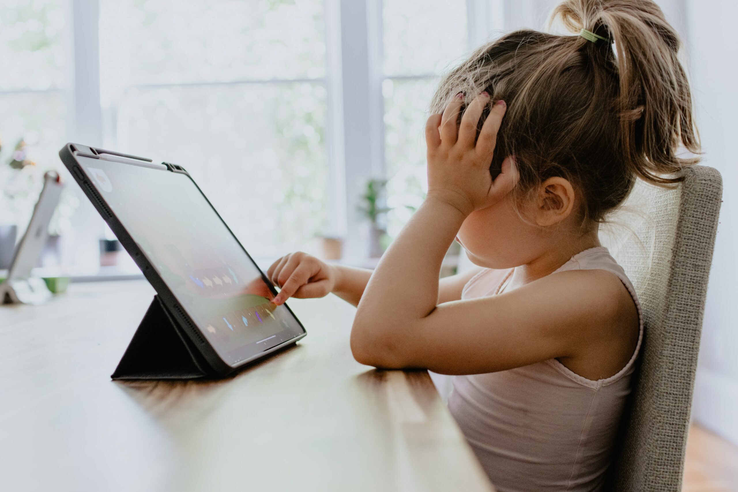 A young child sits at a table using a tablet.