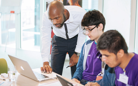 An educator helps a young person with a computing problem.