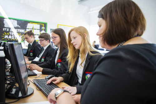 Teenage students and a teacher do coding during a computer science lesson.