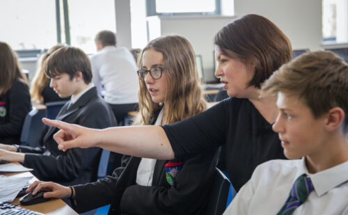 Teenage students and a teacher do coding during a computer science lesson.