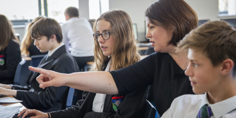 Teenage students and a teacher do coding during a computer science lesson.