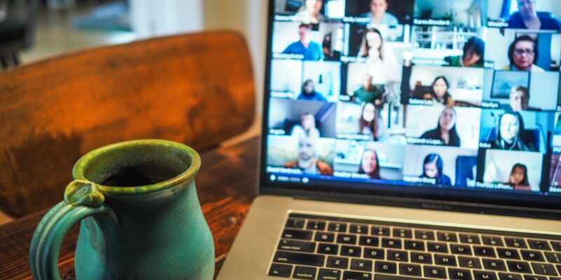 An earthenware mug next to a laptop showing a grid of video call participants.