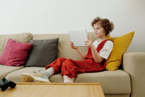 A girl has fun learning to code at home on a tablet sitting on a sofa.