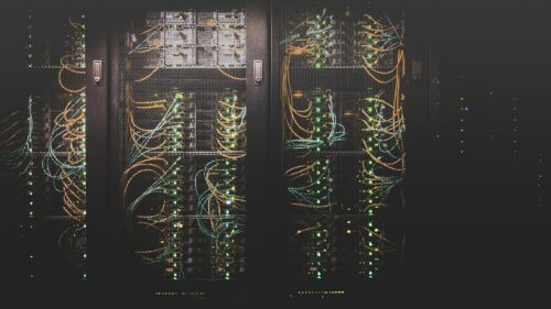 Stacks of server hardware behind metal fencing in a data centre.