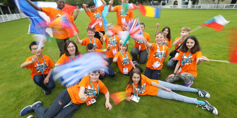 A group of Coolest Projects participants from all over the world wave their flags.