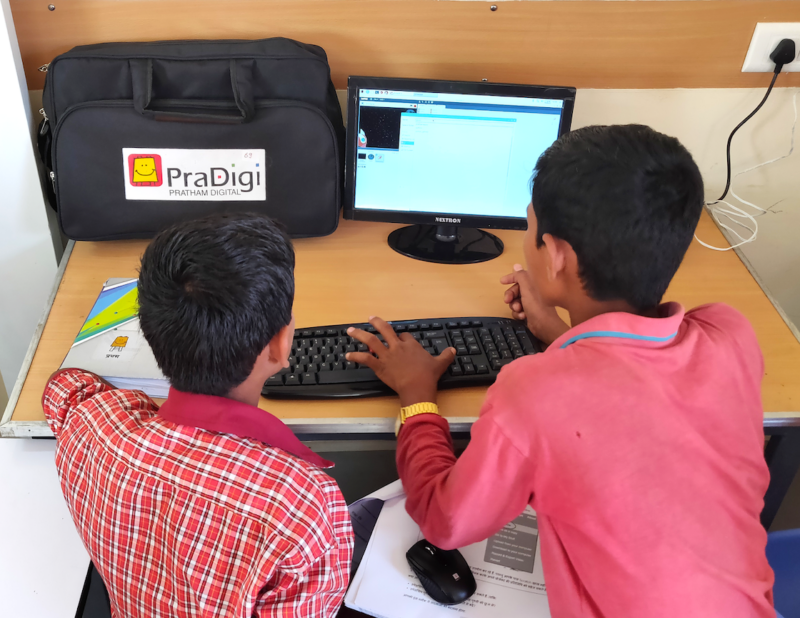 Two boys use a PraDigi computer at a desk.