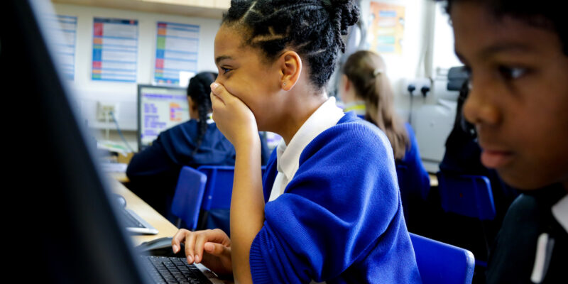 In a computing classroom, a girl laughs at what she sees on the screen.