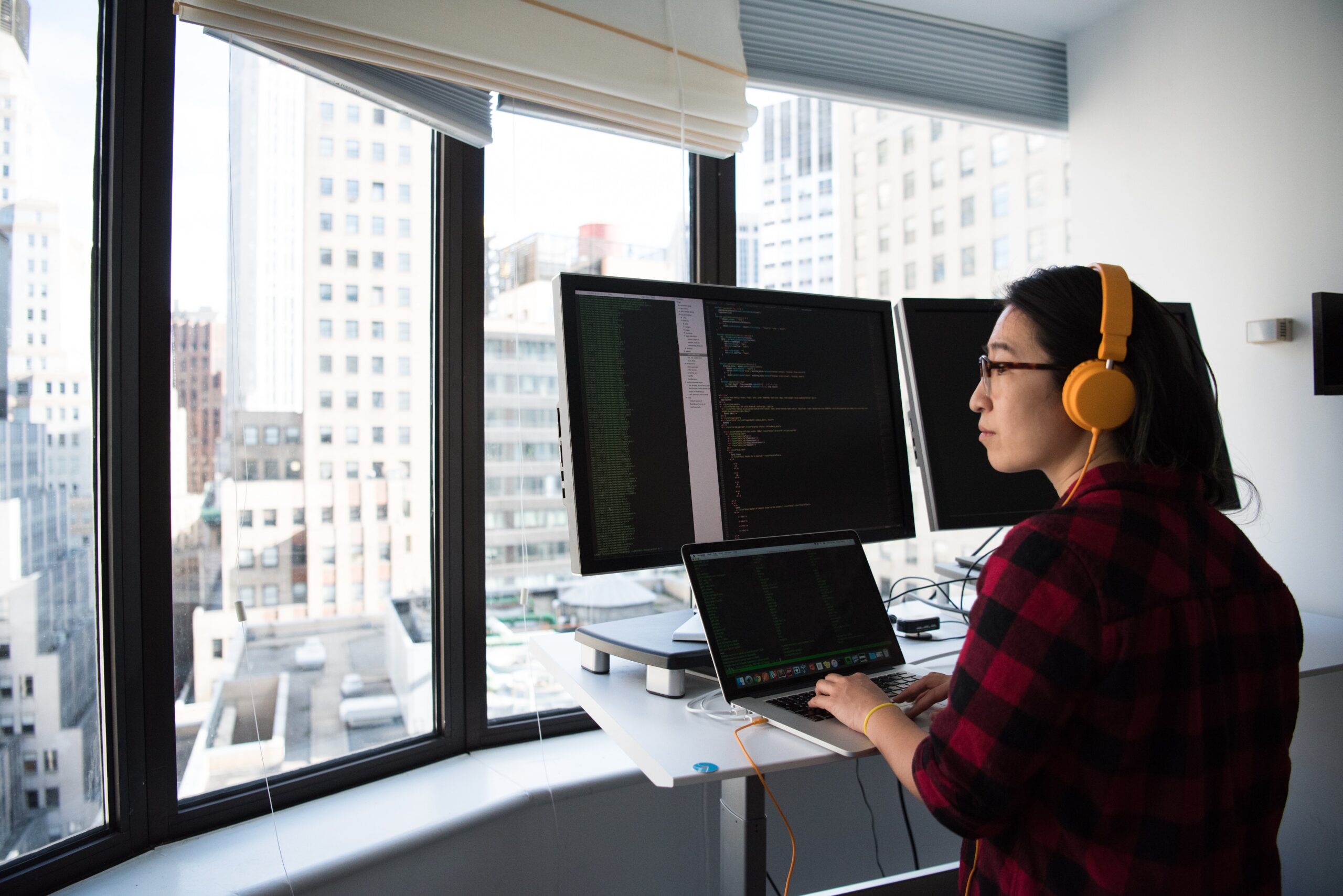 A woman works at a multi-screen computer setup on a standing desk.
