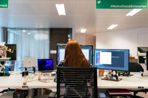 A woman works at a multi-screen computer setup on a desk.