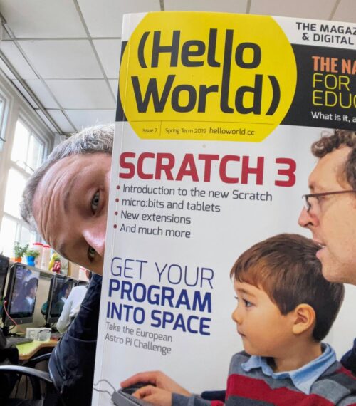 An educator holds up a copy of Hello World magazine in front of their face.
