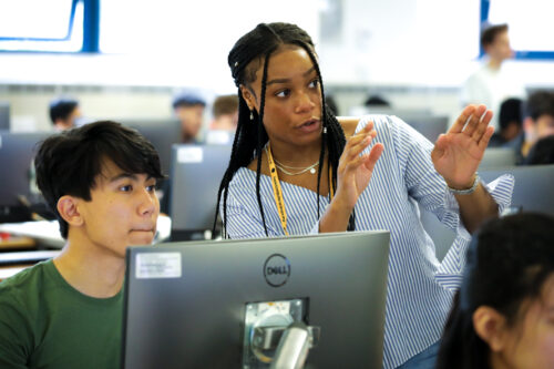 A teacher explains something to a learner in a computer science class.