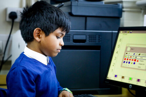 In a computing classroom, a boy looks down at a keyboard.