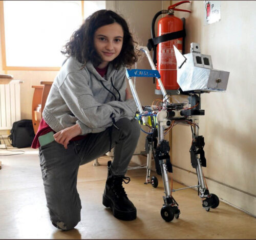 Selin is posing on one knee, next to her robot.